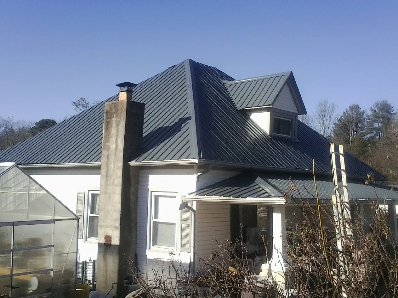 Dark blue standing seam metal roof on a white farmhouse with dormer — Slate & Tile Roof Repair by Roofing Brothers in Astatula